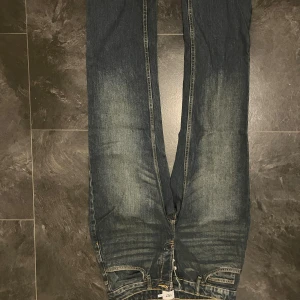  512 blå jeans med raka ben - Säljer ett par Levis 512 jeans i klassisk blå tvätt med snyggt slitna detaljer och raka ben. Jeansen har fem fickor, kontrastsömmar och en cool vintagekänsla. Perfekta för dig som gillar en tidlös och avslappnad look.
