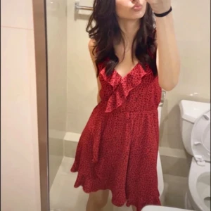 Röd leopardmönstrad volangklänning - Snygg röd kortklänning med svart leopardmönster och volangdetaljer framtill. Klänningen har smala axelband, v-ringning och markerad midja. 