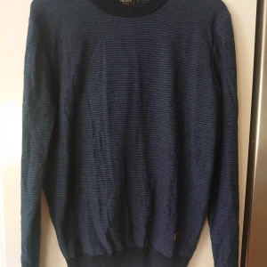 Randig marinblå tröja från Pepe Jeans, 50 % merinoull  - Säljer en randig marinblå tröja från Pepe Jeans i storlek L. Tröjan är stickad i en mix av 50% merinoull och 50% akryl, har rund hals och långa ärmar. Perfekt för dig som gillar en klassisk och stilren look med en chill vibe.
