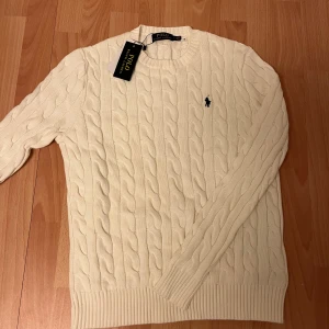 Stickad Polo Ralph Lauren tröja - Stickad vit tröja från Polo Ralph Lauren med klassisk rund hals och broderad logga på bröstet. Perfekt för en clean och stilren look. Priset är inte hugget i sten! Hör av dig vid minsta fråga!