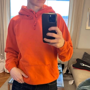 Orange hoodie från BikBok med huva - Säljer en orange hoodie från BikBok i storlek S. Tröjan har en klassisk huva med snörning, magficka och ribbade muddar vid ärmslut och nederkant. Lite nopprig annars fint skick!