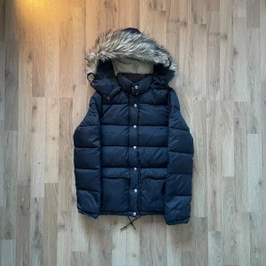 Svart pufferjacka från Ralph Lauren XS - Svart pufferjacka från Ralph Lauren med avtagbar huva och snygg fuskpäls. Jackan har dragkedja och knappar framtill, snörning i nederkant och två stora fickor. Insidan är beige och materialet är polyester. Perfekt för kalla dagar.  Bilder på måtten finns tillgängliga. Fråga gärna! Snabb leverans!