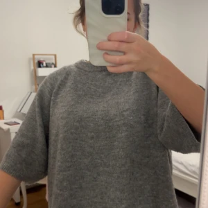 Grå stickad tröja från 1951, S - Mysig grå stickad tröja från Lager 157 i storlek S. Tröjan har en rund hals och korta ärmar, perfekt för lager-på-lager under kyliga dagar. Den har en loose passform och är tillverkad i ett mjukt stickat material som känns skönt mot huden.