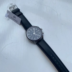 Klocka - BUTIKSPRIS 3049kr. Stilren kronografklocka från Valmont med svart urtavla och silverfärgade detaljer. Klockan har svart läderarmband och boett i silverfärgad metall. Urtavlan har flera små visare och tachymeter-skala runt kanten. Perfekt accessoar för en modern look. PRISET KAN DISKUTERAS.