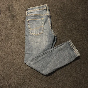 Blå jeans från Jack & Jones - Snygga blå jeans från Jack & Jones med klassisk femficksdesign och kontrastsömmar. Modellen har rak passform och normal midja, tillverkad i mjukt denimtyg som är skönt att bära. Perfekt för dig som gillar stilrena och tidlösa jeans.