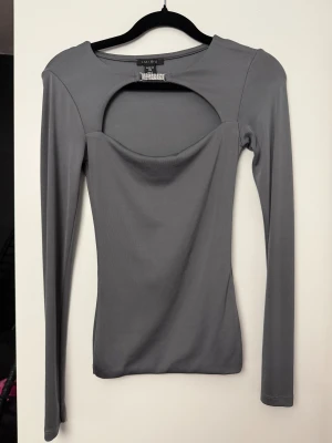 Grå långärmad topp med cut out - Snygg grå långärmad topp från MISU med unik cut out-detalj vid bröstet och en liten glittrig detalj vid halsringningen. Toppen har en tight passform och är tillverkad i ett stretchigt, mjukt material som sitter skönt på kroppen.