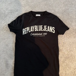 Svart Replay t-shirt med tryck - Svart t-shirt från Replay med stort vitt tryck 'REPLAY BLUE JEANS Established 1981' på bröstet. Klassisk rund hals och korta ärmar. Skön och mjuk bomullskvalitet som passar perfekt till jeans eller shorts. Snygg streetstil för dig som gillar tydliga loggor.