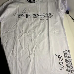 Pop Smoke x Vlone vit t-shirt - Snygg vit t-shirt från Vlone med Pop Smoke-tryck på framsidan och stor V med Faith-text på ryggen. T-shirten har korta ärmar och är gjord i mjuk bomull. Perfekt för dig som gillar streetwear och vill sticka ut med coola prints.