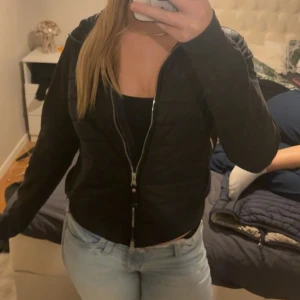 Svart pufferjacka från Parajumpers - Köpte jackan för 5000kr, men andvänt bara några få gånger. Svart pufferjacka från Parajumpers med quiltad front och släta ärmar. Jackan har en hög krage med gul och orange detalj, samt patch på ärmen. Dragkedja framtill och sidofickor med zip. 