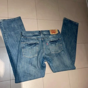 Levi's 501 jeans - Klassiska Levi's 501 jeans i blå tvätt med raka ben och fem fickor. Jeansen har knappgylf, ikonisk patch bak och röd Levi's-tag på bakfickan. Perfekt för dig som gillar tidlös stil och vill ha ett par jeans med autentisk känsla.