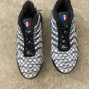 Nike Air Max sneakers svart/vit mönster - Nike Air Max sneakers med svart och vit rutigt mönster, svarta snören och detaljer. Snygg sula med synlig Air Max-dämpning och cool fransk flagga på plösen. Perfekta för dig som vill sticka ut med en unik och sportig look.