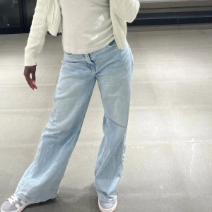 Ljusblå wide jeans med slitna benslut - Säljer ett par ljusblå jeans med bred passform och raka ben. Byxorna har ett sett på siden som ör en del av designen 