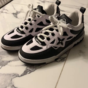  svartvita sneakers - Snygga i svart och vitt med coola detaljer och logotyp på sidan. Skorna har snörning, rund tå och platt sula. Materialet är en mix av skinn och syntet med meshpartier för extra komfort. Perfekta för dig som vill sticka ut med lyxig streetstyle.