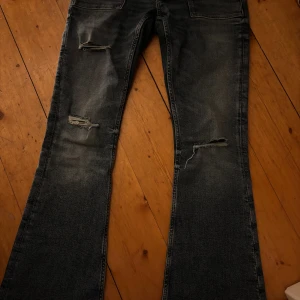 Blå bootcut jeans från Gina Tricot - Snygga blå jeans från Gina Tricot i bootcut-modell med slitna detaljer och två knappar i midjan. Jeansen har klassiska fickor fram och bak, samt en låg midja. Materialet är jeans med en mörk tvätt och coola slitningar på benen. Knapptast använda då de inte riktigt va min stil. Sitter bra på mig som har allt ifrån 34-38 i byxor. PRIS GÅR ATT DISKUTERAS!❣️