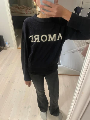 Mörkblå stickad tröja med AMORE - Snygg mörkblå stickad tröja från Gina Tricot med vit text 'AMORE' framtill. Tröjan har en klassisk rund hals och långa ärmar.