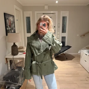 Grön trenchcoat med bälte - Säljer denna gröna trenchcoat med bälte. Helt ny med prislapp