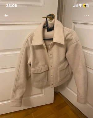 Beige teddyjacka från Vero Moda - Säljer en beige teddyjacka från Vero Moda i storlek M.  stora fickor framtill och klassisk krage. Materialet är mjukt. Stängs med knappar framtill och har långa ärmar.