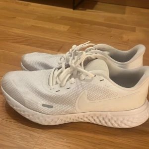 Vita Nike sneakers med snörning - Säljer ett par helvita Nike sneakers med klassisk swoosh på sidan. Skorna har snörning och en tjock, mönstrad sula som ger bra grepp. Passar till löpning eller vardag. Inte använda så mycket så de är väldigt fina. 