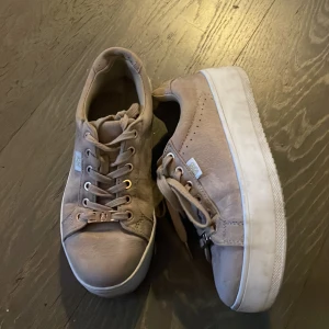 Beige sneakers med plattformssula - Snygga beige sneakers från Pernilla Wahlgren med plattformssula och rund tå. Skorna har snörning med metallöglor i roséguld och en liten vit etikett med glitterdetalj på sidan. Ovandelen är i mocka och sulan är vit och rejäl för extra höjd. Använda men fint skick utan defekter alls. Rengörs fint innan köp. Använd gärna köp nu