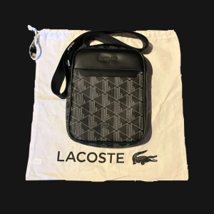Lacoste vertical camera bag   - Lacoste Vertical Camera bag unisex - noir/gris. Nypris 1600kr. Bara skriva om du undrar något 
