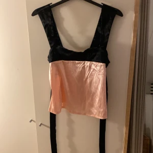 Svart och rosa korsettopp i satin från SHEIN  - Unik korsettopp från SHEIN med breda svarta axelband och knytband i ryggen. Toppen är i glansigt rosa satinmaterial framtill och har en snygg kontrast mellan svart och rosa. Perfekt för dig som vill sticka ut med en cool och trendig look.