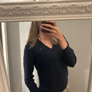 Mörkblå v-ringad tröja från Gant - Snygg mörkblå v-ringad tröja från Gant med diskret logga på bröstet. Tröjan har lång ärm och är tillverkad i mjuk bomull som känns skön mot huden. 