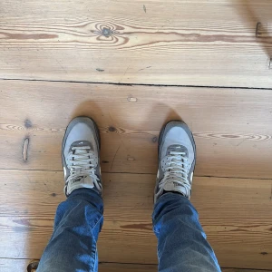  Air Max 90 grå sneakers - Säljer ett par Air Max 90 sneakers i olika grå nyanser med vita detaljer och svart sula. Skorna har klassisk snörning, rund tå och den ikoniska Air Max-detaljen i sulan. Ovandelen är i mesh och mocka för en snygg och sportig look.