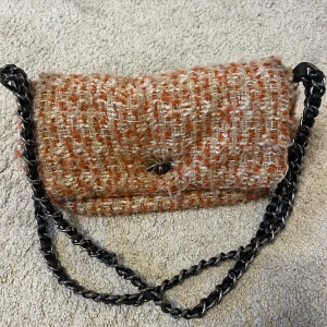 Beck södergård väska - Säljer en snygg axelväska i beige och orange tweed med silverfärgad kedjerem. Väskan har ett rutigt mönster och stängs med ett coolt metallspänne framtill. Lite trasig vid spännet som man kan se på bilden 🧡