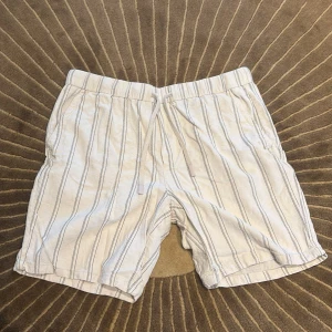 Randiga Zara-shorts i linne - Snygga ljusbeige shorts från Zara med svarta ränder. Modellen har elastisk midja med snörning och fickor både fram och bak. Materialet är linne, vilket gör dem luftiga och perfekta för varma dagar. Passformen är normal.