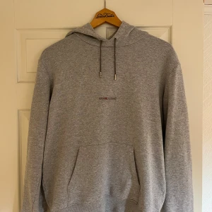  Saint Laurent hoodie  - Snygg grå hoodie från Saint Laurent med diskret logga på bröstet. Tröjan har huva med snörning, stor känguruficka och ribbade muddar. Perfekt för dig som gillar stilrena och exklusiva plagg med streetkänsla.