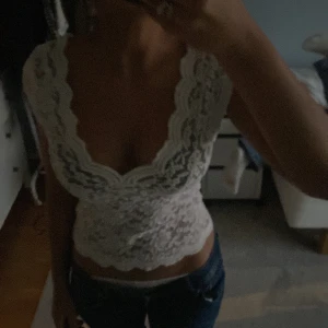 Vit spetstopp  - Säljer en vit blus i spets med djup v-ringning och korta ärmar ifrån stradivarius. Toppen är croppad och har ett romantiskt blommigt spetsmönster samt vågig kant nedtill. den har ett litet hål vänstra sidan men det synns knappt.