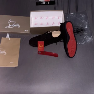 Svarta sneakers från Christian Louboutin - Snygga svarta sneakers från Christian Louboutin i lyxig mocka med den ikoniska röda sulan och rund tå. Skorna har svarta snören och eleganta, diskreta sömmar som ger ett stilrent och exklusivt uttryck. Insidan är klädd i ljusbeige med en guldfärgad logga som förstärker den exklusiva känslan.  Köpta i storlek 46, men de är stora i passformen – motsvarar snarare storlek 47. Perfekta för dig som uppskattar premiumkvalitet och tidlösa detaljer.