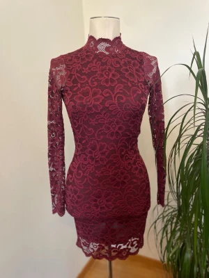 Vinröd spetsklänning från Bik Bok Ny - Supersnygg vinröd kortklänning från Bik Bok med blommigt spetsmönster, långärmad och figurnära passform. Klänningen har hög hals och öppen rygg. Perfekt för dig som vill sticka ut med detaljer som spets och blommor. 