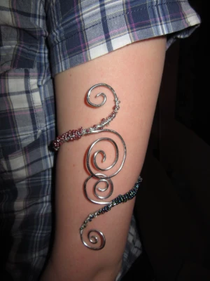 Spiralformad silverfärgad armcuff - Unik spiralformad armring i silverfärgad metall med detaljer av små pärlor i lila och mörkblå. små små repor av tången kan finnas men är inget man tänker på.