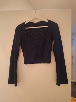 Svart mesh topp från Nelly - Säljer en svart långärmad mesh topp från Nelly i storlek S. Toppen har croppad passform, fyrkantig ringning och ett diskret mönster i tyget som ger en cool struktur. Perfekt att styla med jeans eller kjol för en trendig look.