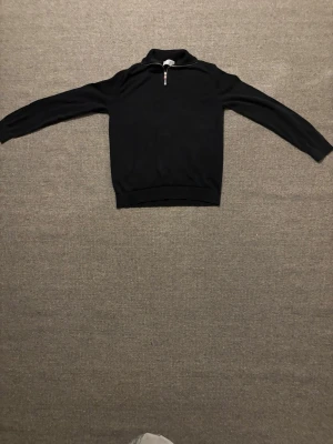 Svart half zip stickad tröja Selected - Svart stickad tröja från Selected Homme med half zip och hög krage. Tröjan har lång ärm och klassisk passform, perfekt till höst och vinter. Enkel och stilren design som funkar till det mesta. Dessvärre har den ett litet hål i armhålan men inget som syns om du inte har händerna i luften kan även snabbt sys ihop 