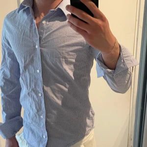 Blårutig skjorta från Riley  - Snygg blårutig skjorta från Riley i slim fit-modell. Skjortan har klassisk krage, långa ärmar och knäppning framtill. Riktigt bra skick!