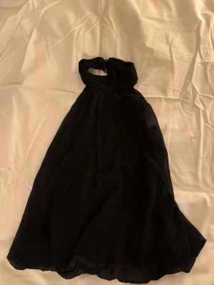 Svart halterneck topp från Nelly - Säljer en svart halterneck till från Nelly i storlek 36. Toppen har en halterneck med knäppning i nacken och ett luftigt, svepande tyg som ger en elegant siluett. Perfekt för dig som gillar stilrena och klassiska plagg.