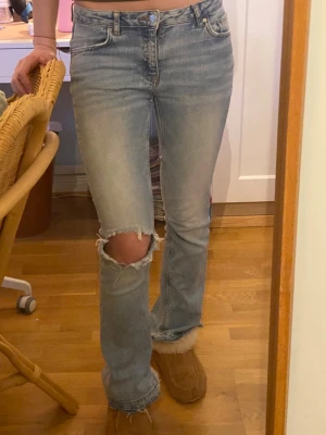 Bootcut ljusblå jeans med hål - Säljer ett par ljusblå bootcut jeans från Gina Tricot med slitningar och ett stort hål på ena knät.💕Jeansen är storlek 158 från Gina Young men de är mycket större på. Jag har sprettad upp sömmen på jeansen där nere för att de skulle bli längre. Därför är de väldigt fransiga längst ner men det gör dem bara coolare! Under ena bakfickan finns en fläck (se bild 5) men den syns inte när man väl har på sig dem. Säljer då de är lite för korta för mig som är 177!☺️
