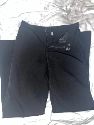 Svarta kostymbyxor från Stories, stl 34 - Snygga svarta kostymbyxor från Stories i storlek 34. Klassisk rak passform med bälteshällor, knapp och dragkedja fram. Byxorna har diskreta fickor bak och är gjorda i ett mjukt material som känns bekvämt hela dagen.