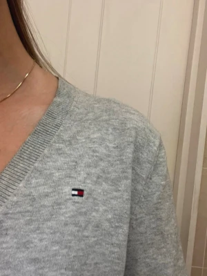 Grå v-ringad tröja Tommy Hilfiger - Snygg grå v-ringad tröja från Tommy Hilfiger med diskret logga på bröstet. Tröjan har lång ärm och ribbade muddar vid hals och ärmslut. Perfekt för dig som gillar enkel och stilren design. Priset kan diskuteras 🩷🩷🩷🩷