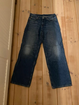 Weekday Ample Low Loose Jeans blå - Säljer ett par Weekday Ample Low Loose Jeans i klassisk blå tvätt. Modellen har låg midja och riktigt loose passform med breda ben. Jeansen är tillverkade i bomull och har fem fickor samt knapp och dragkedja framtill. Perfekt för dig som gillar avslappnad stil. Nästan helt oanvända.