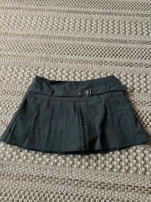 Minikjol Zara - Snygg mörkgrå minikjol med plisserade veck och ett dekorativt bälte i midjan. Kjolen har en smidig dragkedja i sidan och inbyggda shorts.