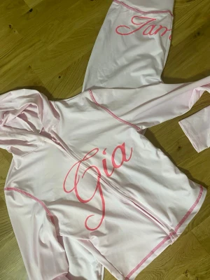 Ljusrosa mjukisbyxor från IamGia - Säljer ett par ljusrosa mjukisbyxor från IamGia med bootcut-snitt och tryckt logga bak på rumpan. Byxorna har en låg midja och är gjorda i mjukt syntetmaterial med stretch. Perfekt för dig som gillar comfy vibes och vill sticka ut med coola detaljer.