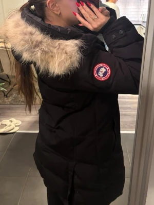 Canada Goose Shelburne Parka Jacka - Säljer en svart jacka från Canada Goose med huva och fluffig pälskant. Jackan har klassisk patch på ärmen, långa ärmar och en rak, lite längre modell. Folk med storlek M, L och XL kan använda den.