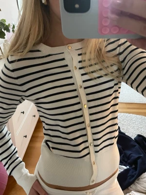 Vit och svart randig kofta med guldknappar - Snygg vit kofta med svarta horisontella ränder och guldiga knappar framtill. Så himla fin och jätteskönt material. Som ny! Storlek xs!