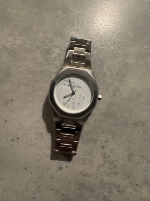 Ny klocka ”Who cares I’m already late” - Bilderna visar en silverfärgad armbandsklocka med metallarmband och en unik urtavla.