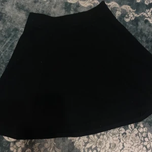 Svart kortkjol från Divided XS - Säljer en svart kortkjol från Divided i storlek XS. Kjolen har en snygg A-linjeform och en synlig dragkedja bak. Materialet är mjukt och stretchigt med bomull och elastan, vilket gör den bekväm att bära. Perfekt att matcha med sneakers eller boots. Den är lite hårig för har katt men kan ta bort det. 