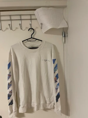 Vit Off-White sweatshirt   - Säljer en vit sweatshirt från Off-White med ikoniska blå och färgglada tryck på ärmarna och stort grafiskt motiv på ryggen. Tröjan har rund hals och är långärmad, tillverkad i mjuk bomull. Perfekt för dig som gillar streetwear och vill sticka ut.Liknande modell som orginala. 