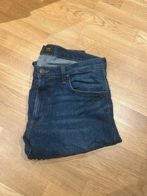 Mörkblå jeans från Lee Luke - Snygga mörkblå jeans från Lee med klassisk femficksdesign och gul kontrastsöm. Jeansen har rak passform och normal midja, tillverkade i slitstarkt bomullsmaterial. Perfekta för dig som gillar en tidlös och enkel stil.